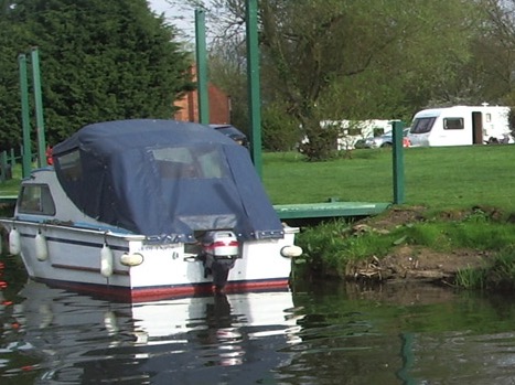 A cabin cruiser moored at a jetty, with touring caravans on the grass behind